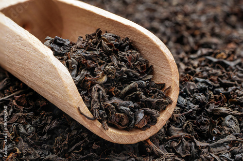 Dry long leaf tea in wooden scoop. Macro of loose black tea.