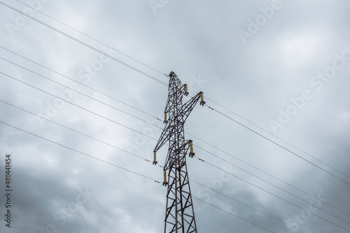 Tall tower of power lines on background of gray cloudy sky. High electric tower with wires against cloudy gray sky. Tower of electricity in overcast. Сloudscape with power lines against gray clouds.