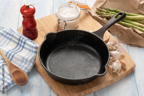 Cast iron skillet on a wooden board with kitchen items.