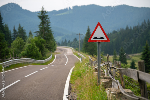 Bumpy road ahead traffic sign on a motorway between the mountains.