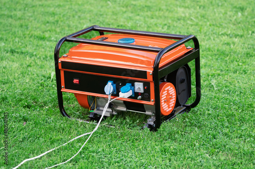 Portable electric generator with electric wires connected on the green grass in summer