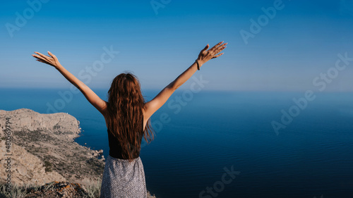 A young woman with her hands up in the fresh air against the background of the sea. Place for your text