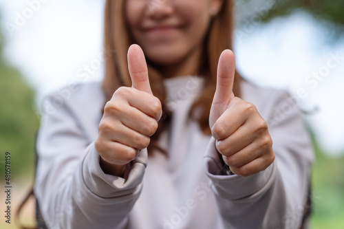 Closeup of a young woman making and showing thumbs up hand sign