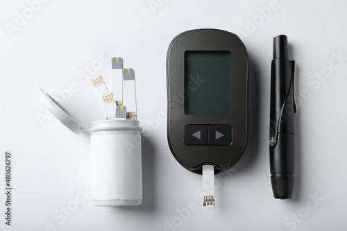 Digital glucometer, lancet pen and test strips on white background, flat lay. Diabetes control