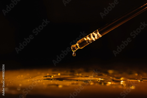 cosmetic pipette with cosmetic oil, perfume, essence, on a black background, gold-colored liquid.
