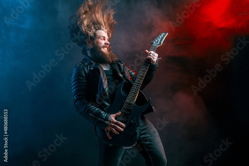 Expression rock guitar player with long hair and beard plays on the smoke background. Studio shot