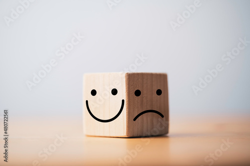 Smile face in bright side and sad face in dark side on wooden block cube for positive mindset selection concept.