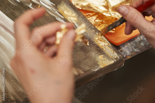 defocused female hands apply gold potal to the picture with a brush