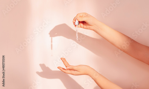 The hands of a young girl with a drop of serum or hyaluronic acid from a pipette on a background. beautiful shade from the sun. Collagen serum drips from the hands of a beautiful woman.