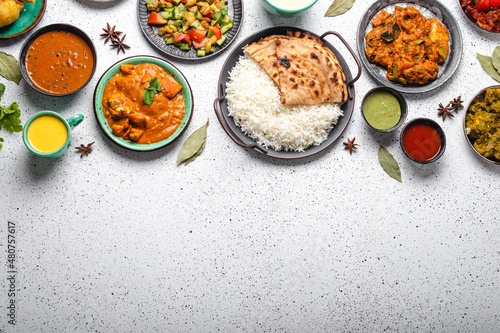 Indian ethnic food buffet on white concrete table top view: curry, samosa, rice biryani, dal, paneer, chapatti, naan, chicken tikka masala, mango lassi, dishes of India dinner background copy space