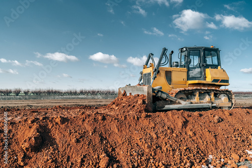 Crawler bulldozer working on construction site or quarry. Mining machinery moving clay, smoothing gravel surface for new road. Earthmoving, excavations, digging on soils.