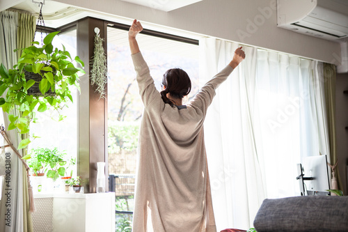 朝、カーテンを開けて伸びをする女性