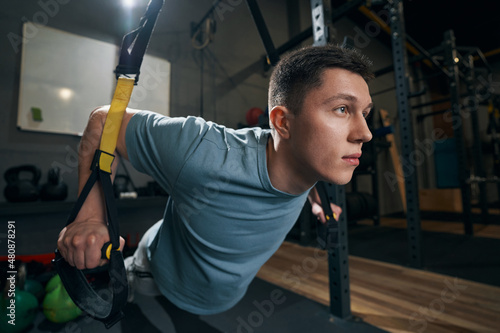 Concentrated strong man exercising on suspension trainer