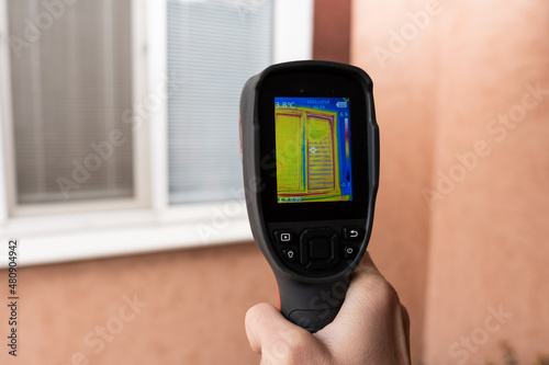 A male hand holds a thermal imager at the window of a house. Search for heat loss in private houses