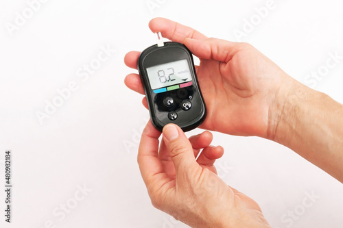 Close-up of the hands of a woman using a glucose meter to measure blood sugar isolated on a white background. Checking blood sugar level by glucometer for diabetes testing. High result, above the norm