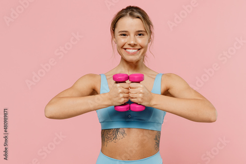 Young strong sporty athletic fitness trainer instructor woman wear blue tracksuit spend time in home gym hold female dumbbells train isolated on pastel plain pink background. Workout sport concept