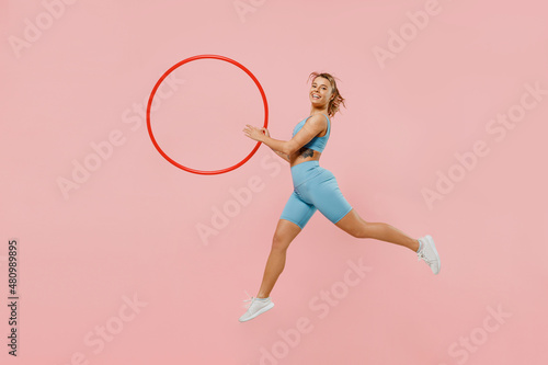 Full body young strong sporty athletic fitness trainer instructor woman wear blue tracksuit spend time in home gym hold hula hoop isolated on pastel plain light pink background. Workout sport concept.