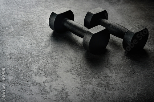 A pair of black dumbbells on a dark concrete background with copy space. The concept of hard training.