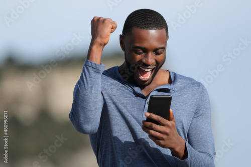 Man with black skin celebrating checking phone