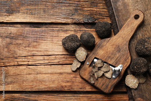 Shaver with whole and sliced black truffles on wooden table, flat lay. Space for text