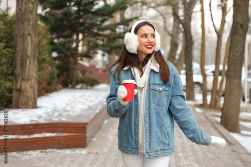 Young woman with paper cup enjoying winter day on city street