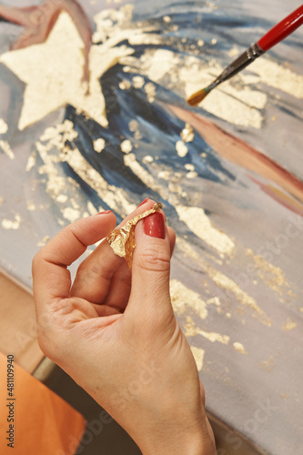female hands transfer the gold potal to the picture, layering it with a brush