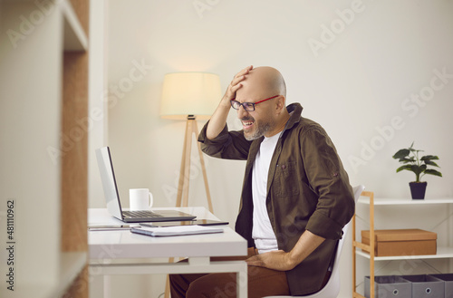 Argh, don't remember it. Middle aged or mature man slaps himself on face while working on laptop computer in home office. Businessman forgets password to his account or makes stupid mistake in project