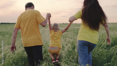 Happy family runs together holding hands in spring, summer. Teamwork. Family weekend. Mom, dad and son are playing on a green wheat field, a happy child is holding parents' hands and jumping.