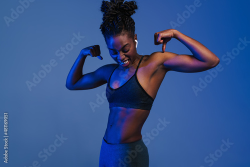 Black young sportswoman in earphones showing her biceps