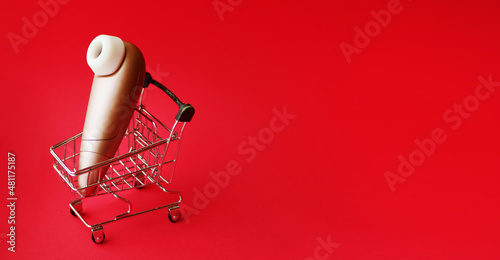 Clitoral vibrator in shopping cart. Sex shop sale banner. Red background. Copy space