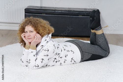 Frau in Sweater mit gefesselten Händen und Füssen, liegt auf Teppich