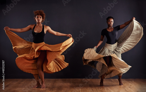 Feminine freedom. Two contemporary dancers with flowing skirts in front of a dark background.