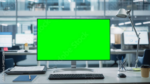 Desktop Computer Monitor with Mock Up Green Screen Chroma Key Display Standing on the Desk in the Modern Business Office. In the Background Glass Wall with Big City Office.