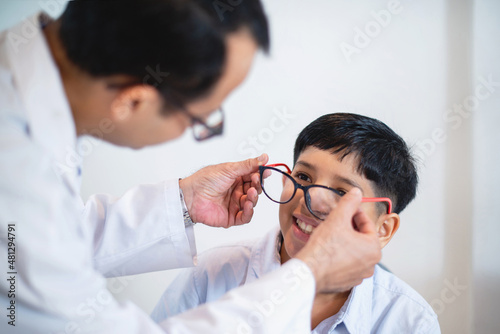 Indian optometrist or optometrist is in white coat helps to get new glasses for boy, child boy in optic store choosing new glasses with optician