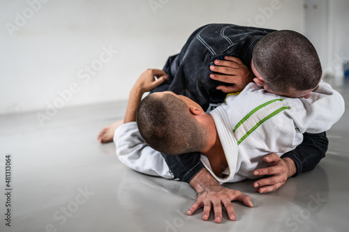 Two brazilian jiu jitsu bjj figters martial arts training male athlete practice technique or sparing at gym on tatami mat wearing black and white kimono gi uniform