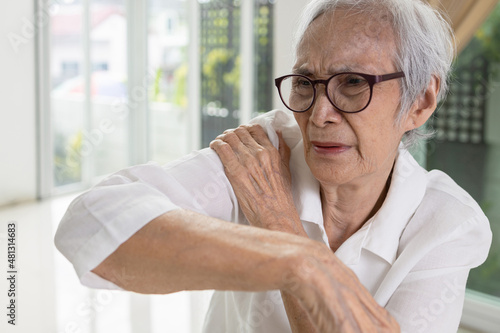 Asian senior woman massage her shoulder bone with hand,aching and tingling,old elderly patient with frozen shoulder,pain and stiffness in the shoulder,degenerative disease,rheumatoid arthritis or gout