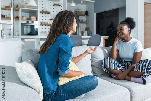 Two young friends and roommates sitting on sofa in their modern cozy studio apartment talking about men. Females conversation about relationships and goals for the future.