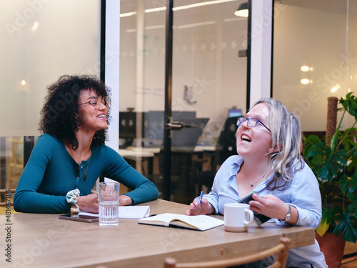 UK, London, Two smiling women writing in notebooks in modern office