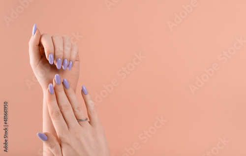 Hands of a beautiful well-groomed with feminine violet lavender nails gel polish on a beige background. Manicure, pedicure beauty salon concept.