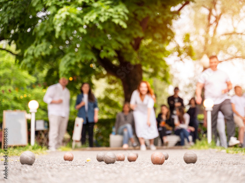 Friends playing bocce game woman through a ball above green trees park in city park in summer sunset light