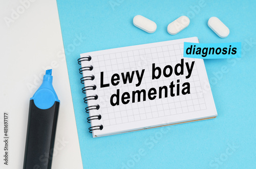 On a white and blue surface are pills, a marker and a notebook with the inscription - Lewy body dementia