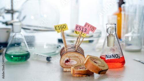 Food additives: sweet roll with chemical additives with colored labels, on a laboratory table. Close up.