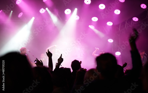 Lighting up you night. Rearview of an audience with hands raised at a music festival and lights streaming down from above the stage.