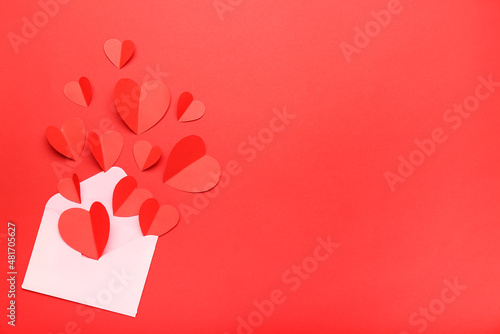 Composition for Valentine's Day February 14. White envelope on a red background with red paper-cut hearts pouring out of it. Flat lay, top view, copy space.