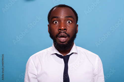 Shocked businessman looking surprised with open mouth facing unbelievable situation on blue background. Amazed person with big eyes jaw dropping. Astonished office worker.