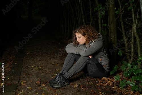 Frau sitzt im dunklen Wald, nachdenklich und deprimiert, Kopf auf die Arme gestützt