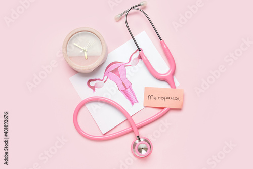 Papers with word MENOPAUSE, uterus, stethoscope and alarm clock on pink background