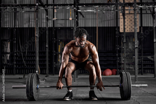 Young muscular african sweaty fit man with big muscles training with heavy barbell weight during cross training workout in modern gym. handsome guy is engaged in sport, fitness, pumping arm muscles