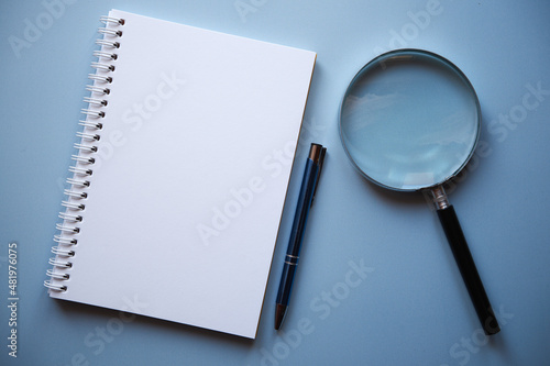 notes, lupa i długopis na niebieskim tle 