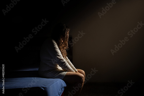 Uma mulher triste, sentada na beirada da cama, de noite. Conceito de depressão.